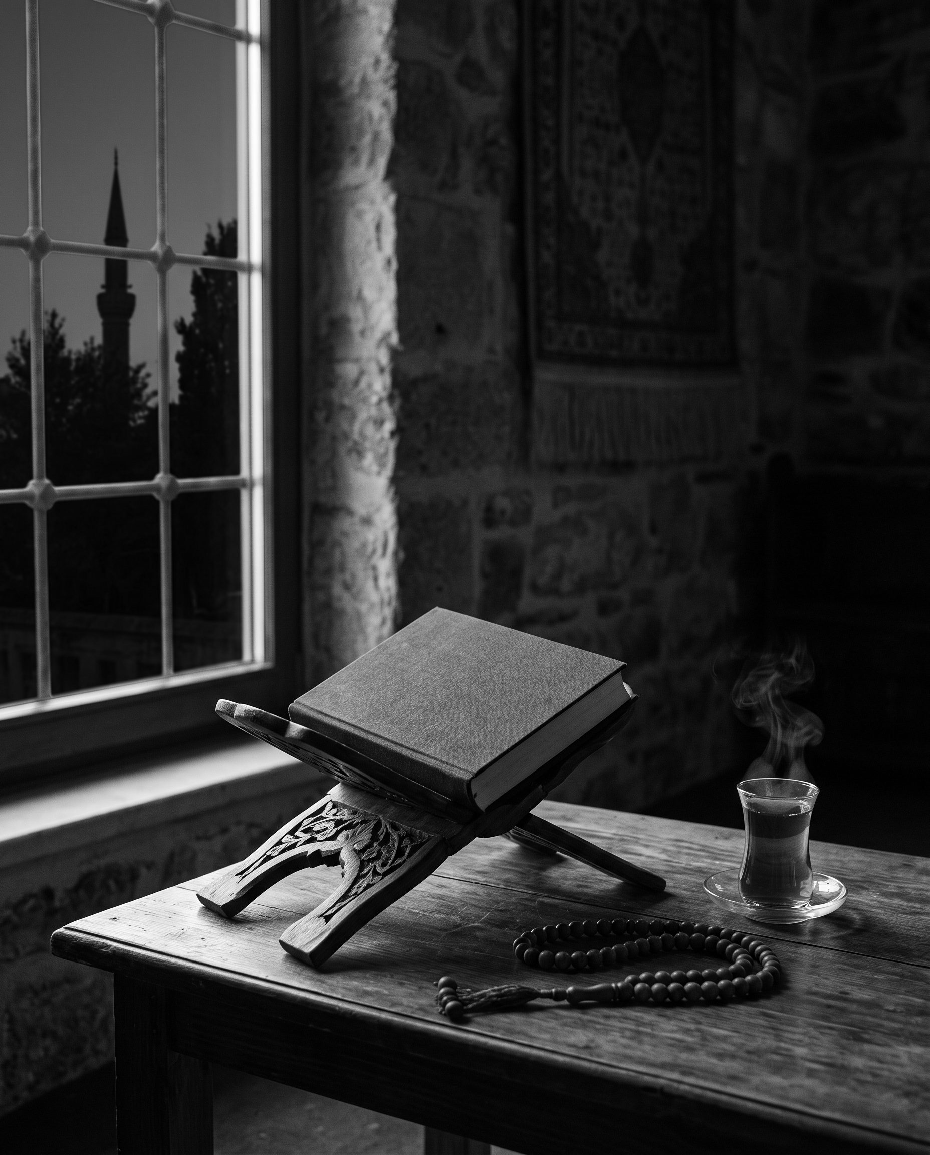 A closed book on a wooden stand beside prayer beads and tea at dawn